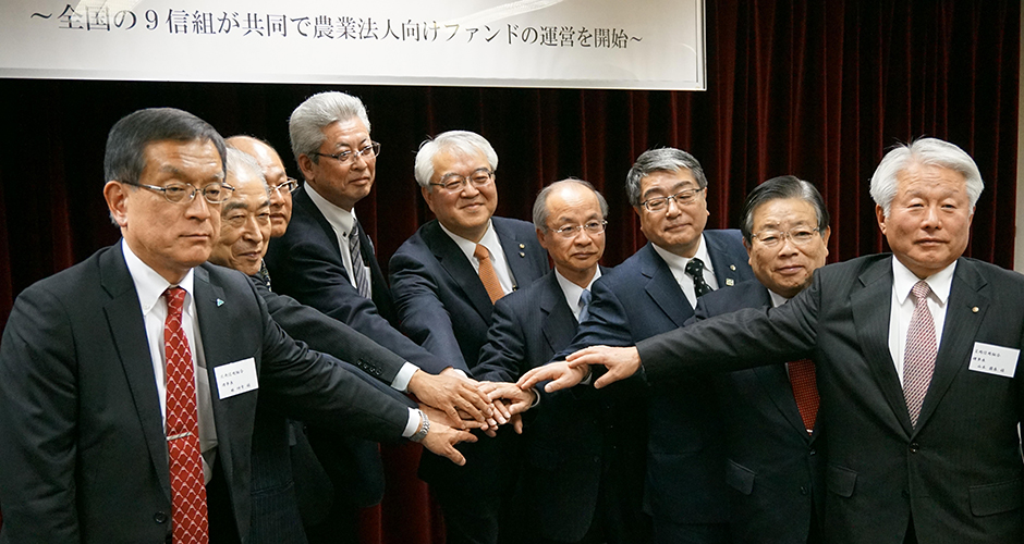 全国の9信用組合が共同で農業法人向けファンドの運営を開始したことを発表する記者会見で、参加者が中央で手を重ね合わせている様子